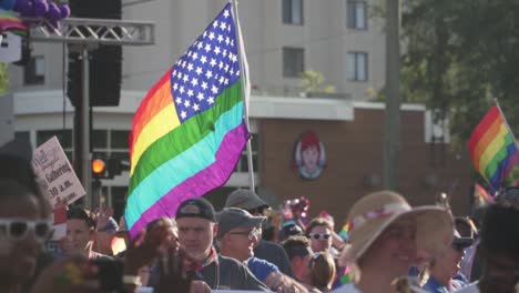 Slow-Motion-Shot-of-American-Gay-Pride-Flag-Waving-in-Air-With-People-Marching-in-Street-at-River-City-Pride-Parade-in-Jacksonville,-FL