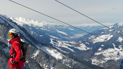 Medium-wide-shot-of-cable-cars-moving-uphill-and-downhill-at-Wagrain-on-a-bright-sunny-day-with-a-man-wearing-skiing-gear-in-the-foreground-and-beautiful-snow-covered-mountains-in-the-background