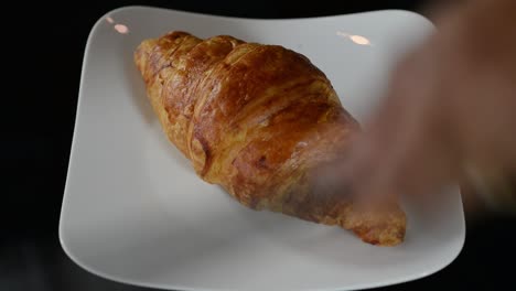A-Croissant-Bread-Placed-On-A-White-Plate-Using-Tongs---close-up