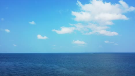 Cielo-Brillante-Con-Nubes-Blancas-Sobre-El-Océano-Azul-Profundo-Y-Un-Barco-Navegando-En-El-Horizonte