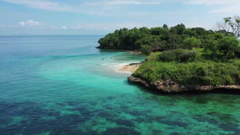 Drone-shot-circling-to-the-left,-revealing-a-small-beach-with-tourists-on-a-beautiful-tropical-island-near-Lombok,-Indonesia