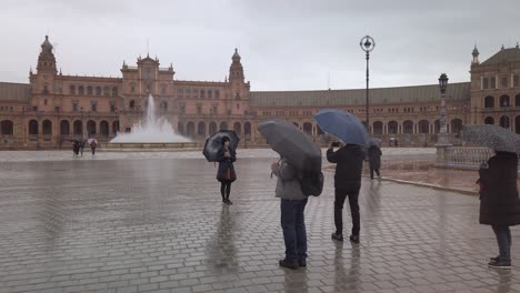 Cámara-Lenta,-Turistas-En-La-Plaza-De-España-Con-Sombrillas-En-Un-Día-Lluvioso,-Sevilla,-España