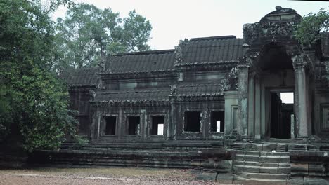 Close-Exterior-Slow-Pan-of-Grey-Ancient-Stone-Entrance-to-Temple-With-Windows-and-Stairs-Surrounded-by-Trees-On-a-Overcast-Cloudy-Day