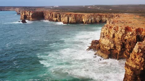 Eroded-sea-cliffs-of-Praia-Do-Tonel-beach-in-Portugal-splashed-by-strong-ocean-waves,-Aerial-flyover-reveal-shot