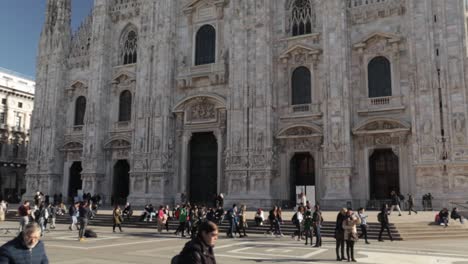 Duomo-cathedral-in-Milan-front-facade-with-tourists,-dolly-out-tilt-up-medium-wide-shot