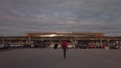 Un-Hombre-Con-Abrigo-Rojo-Y-Mochila-Camina-Hacia-La-Estación-De-Tren-En-Sevilla,-España