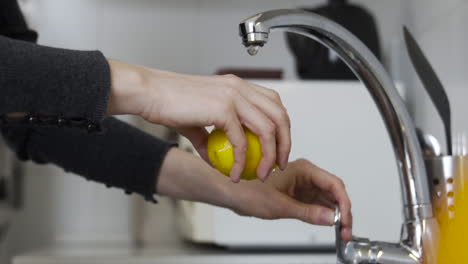 Slow-motion-medium-shot-as-opening-the-tap,-washing-a-lemon-with-running-water