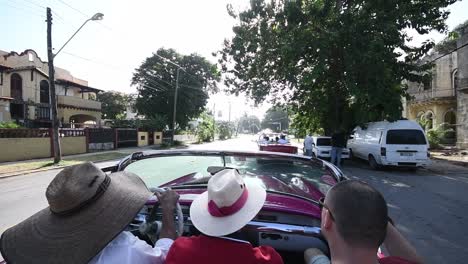 three-close-friends-with-big-cuban-hats-Driving-around-in-a-red-Vintage-Cuban-cabrio-car-in-Havana,-slow-motion
