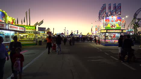 Tracking-Shot-of-People-Walking-Around-at-Florida-State-Fair-With-Food-Stands-and-Rides-in-View-During-Twilight