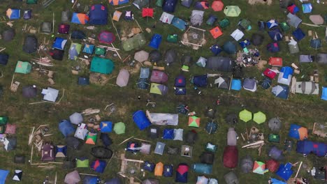 Birds-Eye-Aerial-View-of-Multi-Colored-Tents-Pitched-in-a-Field-at-a-Music-Festival-With-People-Walking-Around