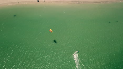 high-altitude-top-down-drone-shot-of-Kite-surfer-in-turquise-Atlantic-ocean-approaching-Langebaan-Beach-in-South-Africa-on-perfect-sunny-weather-in-natural-daylight