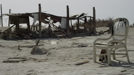 Building-Ruins,-Wood,-and-Abandoned-Chair-Sit-in-Desert-Sand