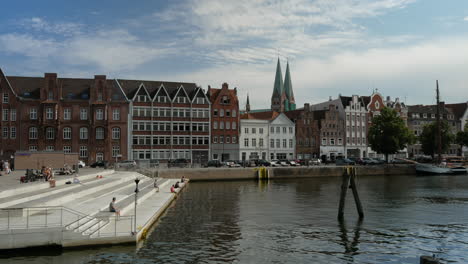 People-enjoying-sun-at-pier-of-Trave-river-with-old-town-architectures-in-background-in-Lubeck