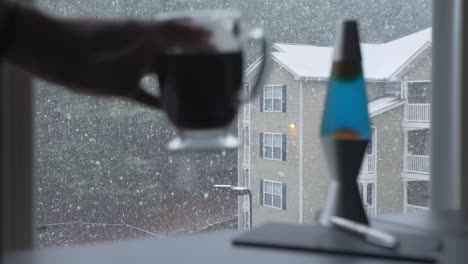 hand-picks-up-glass-coffee-mug-snowing-outside-apartment-building-woodstock-georgia-slow-motion