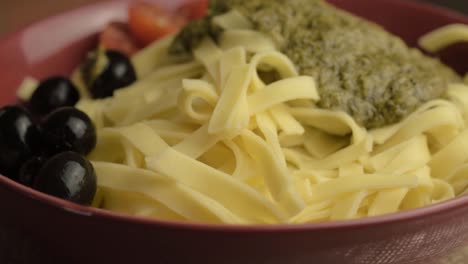 Serving-of-green-pesto-and-tagliatelle-pasta-with-black-olives-rotating-medium-shot