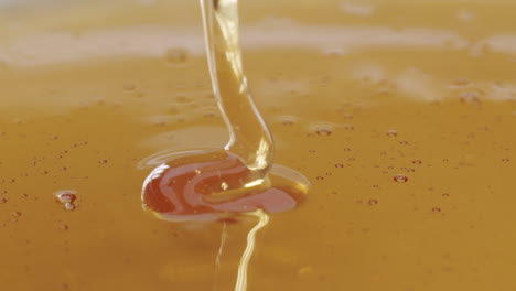 Macro-close-up-shot-of-honey-getting-poured-into-honey-on-a-plane-surface