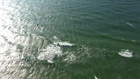 AERIAL:-Locked-Shot-of-Surfers-in-Green-Baltic-Sea-on-Sunny-Bright-Day-in-Natural-Daylight
