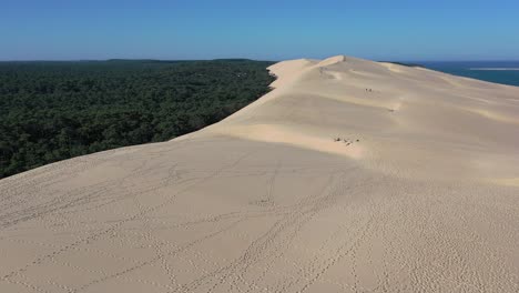 Dune-of-Pilat-in-the-Arcachon-Bassin-France-at-Cap-Ferret-with-a-height-of-110meters-and-people-walking-below,-Aerial-flyover-shot