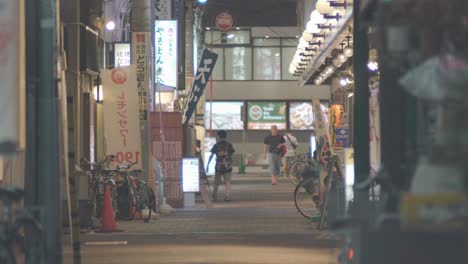Calle-Tranquila-Y-Vacía-Con-Pocas-Personas-Caminando-En-Bicicleta-Por-La-Noche-Durante-La-Pandemia-Del-Coronavirus-En-Kamata,-Tokio,-Japón