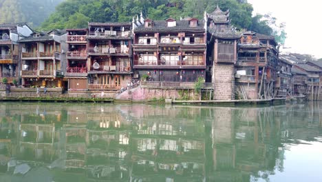 Blick-Auf-Die-Wasserspiegelung-Alter-Historischer-Hölzerner-Diaojiao-Häuser-Am-Flussufer-Des-Tuo-Flusses,-Der-Durch-Das-Zentrum-Der-Altstadt-Von-Fenghuang-Fließt