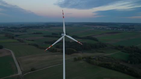 Red-tipped-windmill-overlooking-the-green-landscape-of-Lubawa,-Poland--aerial
