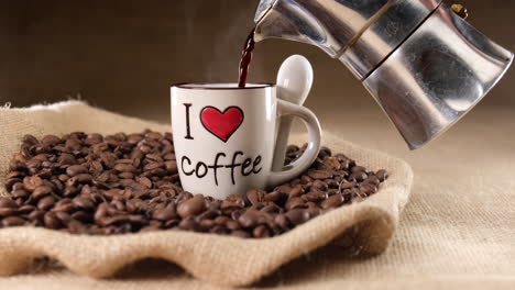Pouring-coffee-on-I-LOVE-COFFEE-cup-from-moka-machine-on-jute-background-and-coffee-beans