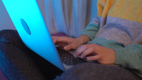 Woman-typing-with-the-computer-on-top-at-night,-she-is-sitting-on-the-bed
