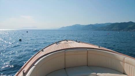 Small-boat-slowly-floating-on-a-calm-sea-in-daylight,-with-mountains-in-the-background,-near-Portofino---Liguria