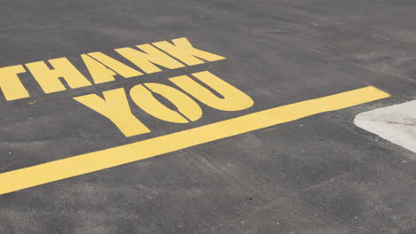 Thank-You-message-painted-in-yellow-on-asphalt-parking-lot-surface-camera-pan-tilt