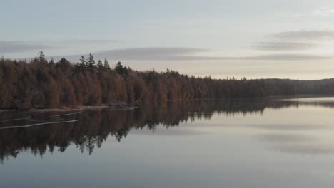 Aerial-Sunrise-over-lake-shoreline-forestry-melting-ice-on-water-surface