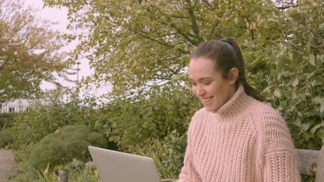 Female-working-on-a-laptop-in-a-park-celebrating-happy