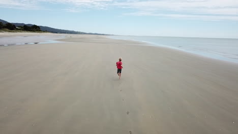 AERIAL-FOLLOWING-shot-of-a-boy-running-along-a-beach