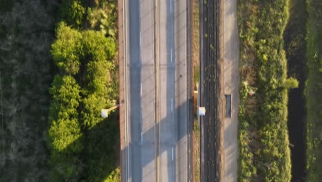 Aerial-top-down-dolly-in-following-a-road-and-railway-cable-stayed-bridge-surrounded-by-vegetation-at-golden-hour