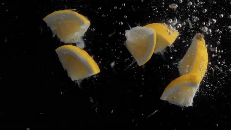 Lemon-Pieces-Falling-into-Water-Super-Slowmotion,-Black-Background,-lots-of-Air-Bubbles,-4k240fps