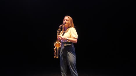 Junge-Musikerin-Spielt-Solo-Auf-Saxophon-Unter-Licht-Auf-Dunkler-Bühne