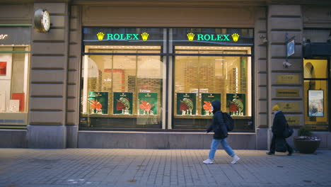 People-walk-past-Rolex-store-with-display-windows-in-Helsinki,-slomo