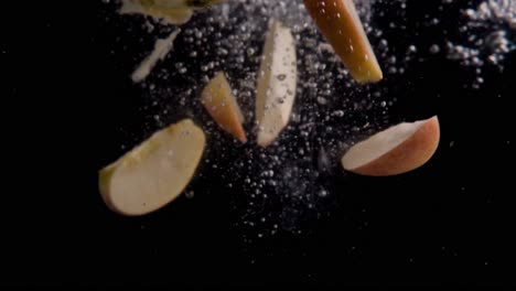 Apple-Slices-Falling-into-Water-Super-Slowmotion,-Black-Background,-lots-of-Air-Bubbles,-4k240fps