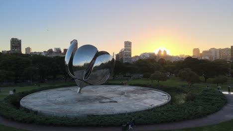 Dolly-in-of-Floralis-Generica-steel-sculpture-in-Naciones-Unidas-square-and-Recoleta-buildings-in-background-at-golden-hour