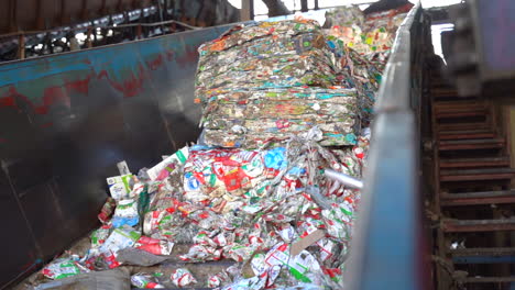 cinematic-shot-of-bales-of-flattened-milk-and-juice-cartons-on-a-conveyor-in-a-recycling-plant-sill-in-bails-of-recycled-material