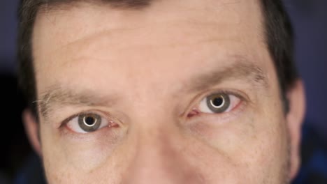 Ein-Mann,-Der-In-Extremer-Nahaufnahme-In-Die-Kamera-Blickt,-Mit-Scharfen-Und-Unscharfen-Augen,-Vor-Einem-Blauen,-Unscharfen-Hintergrund
