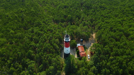 Drone-spinning-around-Stilo-Lighthouse-and-green-forest--lighthouse-located-in-Osetnik-on-the-Polish-coast-of-the-Baltic-Sea,-close-to-the-village-of-Sasino,-aerial