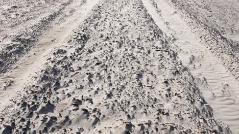Tilt-up-shot-of-tire-marks-of-desert-vehicle-driving-in-sandy-desert-during-sunlight