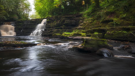 Panorama-time-lapse-of-spring-forest-cascade-waterfall-surrounded-by-trees-with-rocks-in-the-foreground-in-rural-landscape-of-Ireland