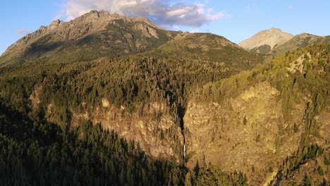 Aerial-dolly-out-over-Corbata-Blanca-thaw-waterfall-hiding-between-pine-tree-forest-mountains-at-sunset,-patagonia-Argentina