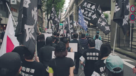 Following-A-Group-Of-Protesters-In-Black-Shirts-Marching-In-The-Street-In-Tokyo---Free-Hong-Kong-Revolution-Now-Message-In-Black-Flag---handheld-shot