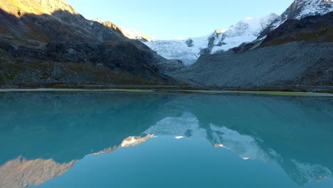 Flying-low-over-small-lake-with-reflecting-mountains-and-glacier-at-sunset-light