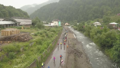 Wide-aerial-shot-of-a-group-of-mountain-bikers-riding-in-the-rain-through-mud-alongside-a-river