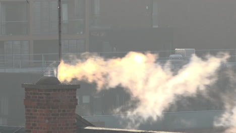 UK-October-2018--Early-morning-sunlight-catches-steam-billowing-from-a-chimney-on-an-old-school-rooftop-in-front-of-newly-built-luxury-apartments-in-East-London