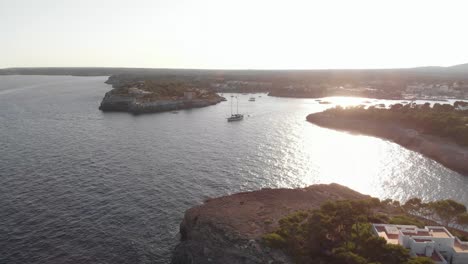 AERIAL:-Mallorca-coast-at-sunset-and-Sail-Yacht-float-out-of-harbor-bay
