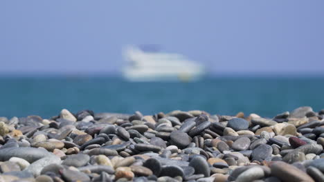 Pebbles-on-sunny-beach-with-blurry-ship-at-sea-zooming-out